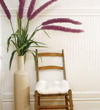 Mur blanc avec lambris et plinthe de couleur blanche. Chaise en bois et grand pouquet de fleurs mauve dans le passage