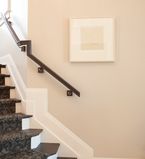 Light beige wall with white baseboards and an oak railing with a oak stair case