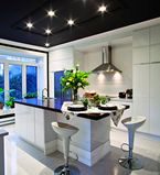 Grande cuisine blanche avec moulure blanche au mur et un planfond gris presque noir avec moulures autour des lumières au plafond.